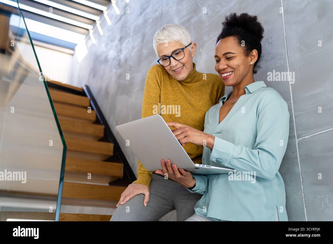 Mentorship and diversity in a modern office as colleagues share a laptop for team collaboration Stock Photo