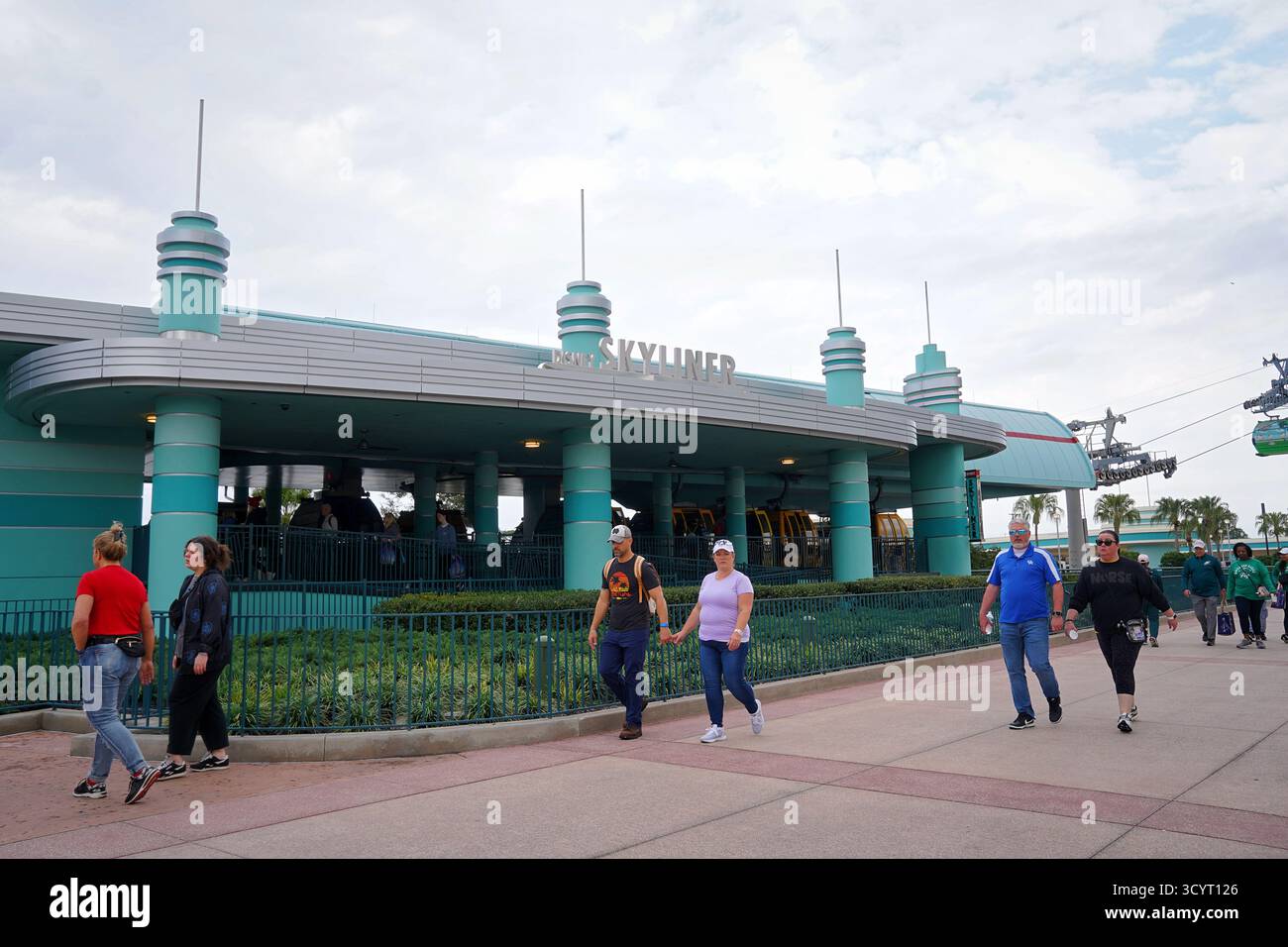 Guests walk toward the Disney Skyliner station at Walt Disney World as gondolas glide overhead on a partly cloudy afternoon Stock Photo