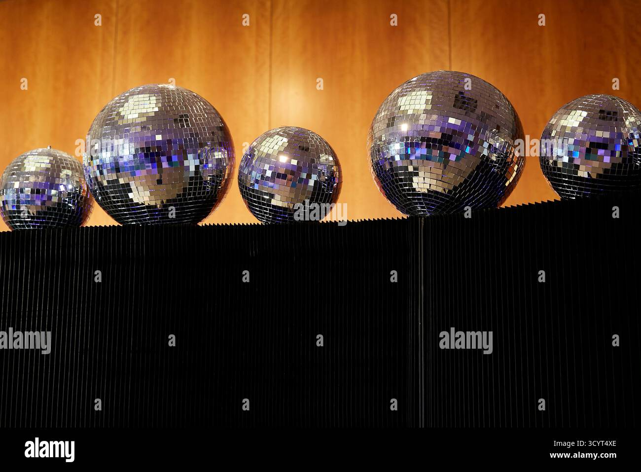 05.09.2025, Germany, Berlin, Berlin - Five mirror balls of different sizes lie on a black partition in front of wood panelling. 00R250905D002CAROEX.JP Stock Photo