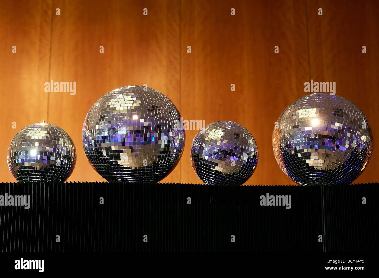 05.09.2025, Germany, Berlin, Berlin - Four mirror balls of different sizes lie on a black partition in front of wood panelling. 00R250905D006CAROEX.JP Stock Photo