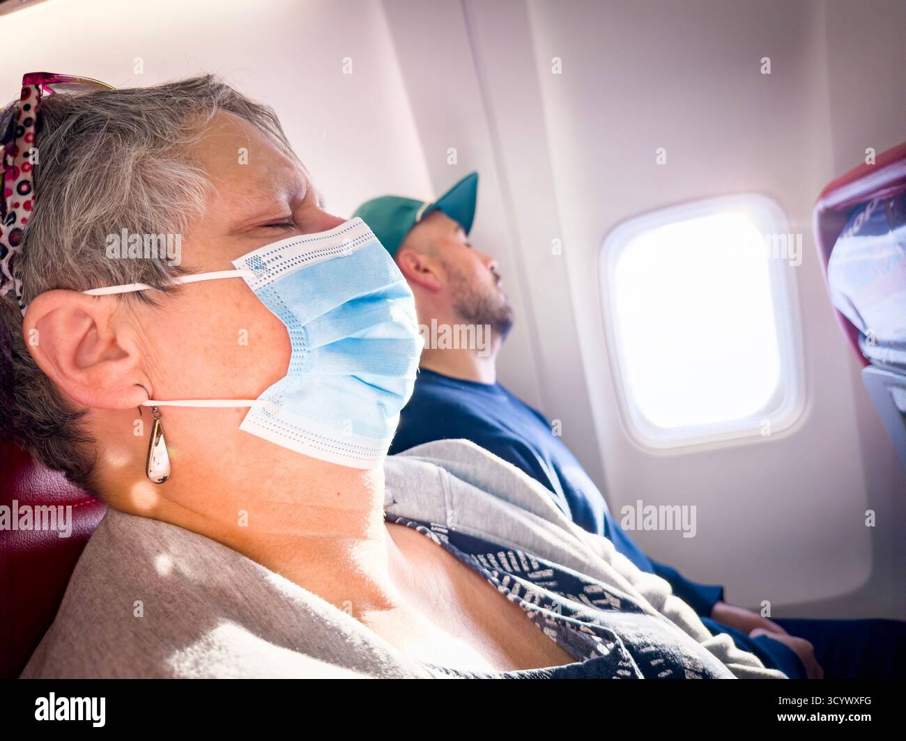 middle aged female Passenger wearing mask sleeping on a jet2 plane during daylight with sunlight coming through the window - Smartphone Captured Stock Image