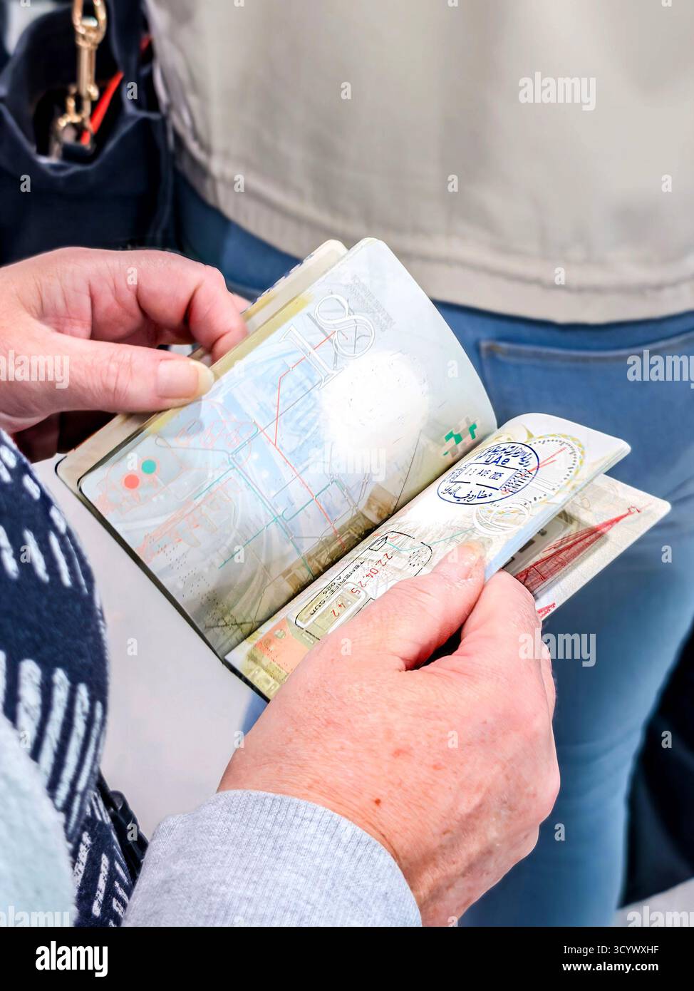 Person holding an open passport with multiple stamps at an airport or border crossing, showing international travel activity - Smartphone Captured Stock Image