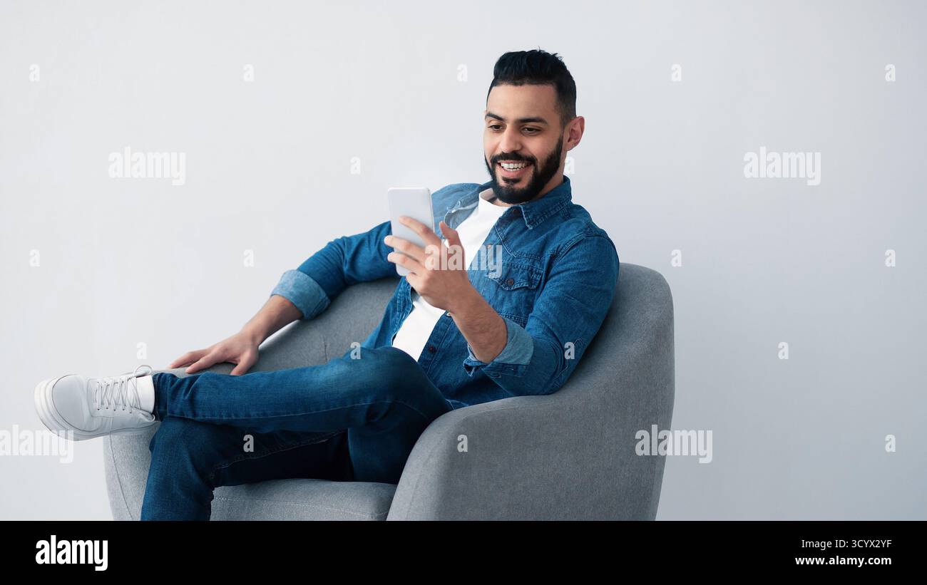 Man Smiling While Using Smartphone in Modern Gray Chair Stock Photo