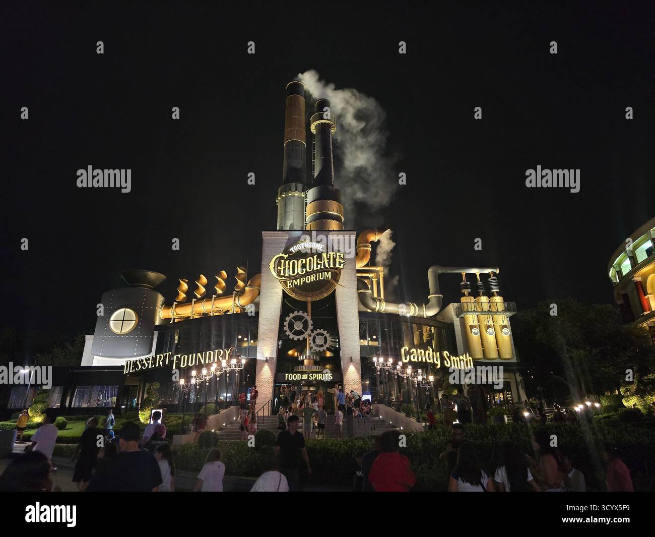 Chocolate Emporium exterior at night. Industrial design, steaming chimneys, and crowds at the popular dessert destination. Chocolate lovers. Florida - Smartphone Captured Stock Image