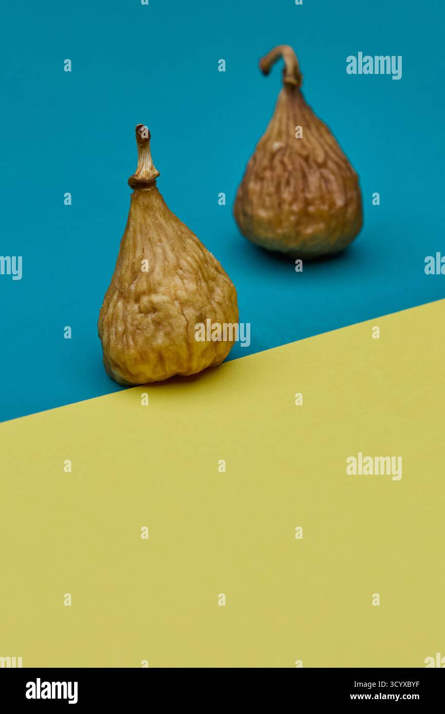Studio image of two dried figs on split blue and yellow surface. Clean composition and natural fruit textures make perfect modern concept for organic Stock Photo