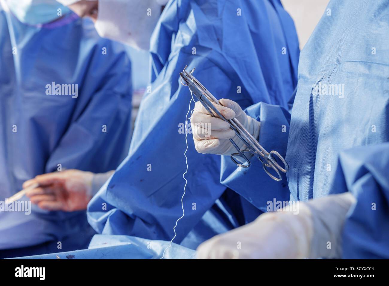 Gloved clinician prepares to suture with a needle holder in a sterile orthopedic operating room, ideal for training, editorial, and medical device use Stock Photo