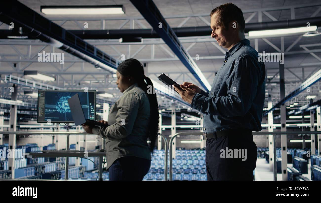 IT expert in server hub uses tablet to optimize deep learning AI systems handling tasks. Data center programmer adjusts artificial intelligence model parameters using device, camera A Stock Photo