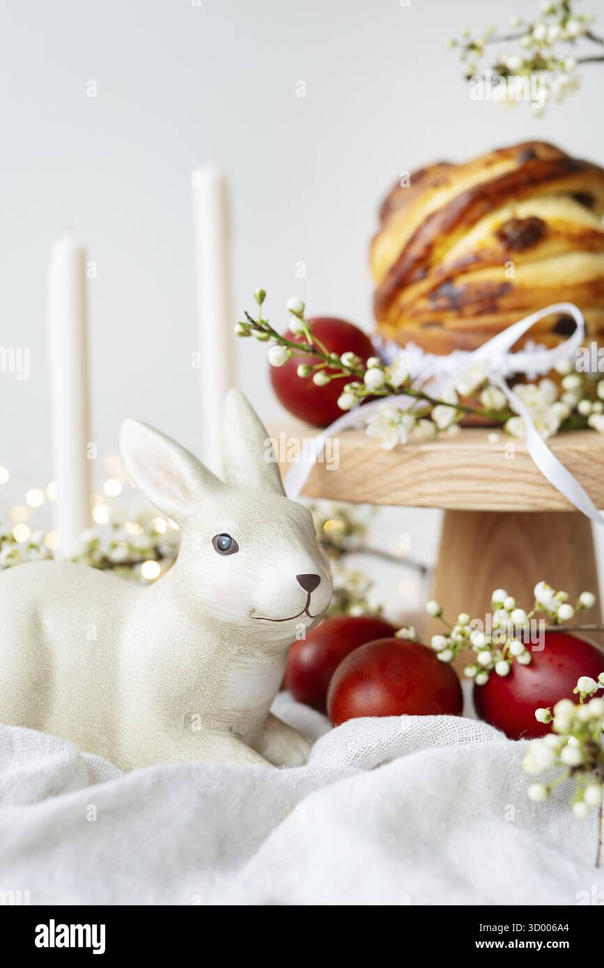 Festive table setting with ceramic bunny, red eggs, candles and Easter pastries. Easter holiday concept Stock Photo