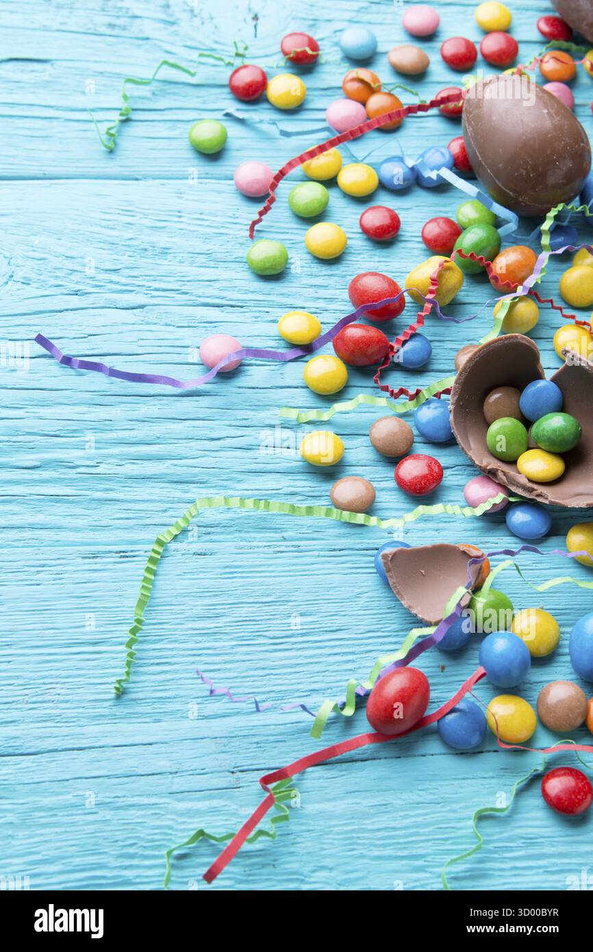 Multicolored dragees, chocolate eggs, ribbons on blue wooden table Stock Photo