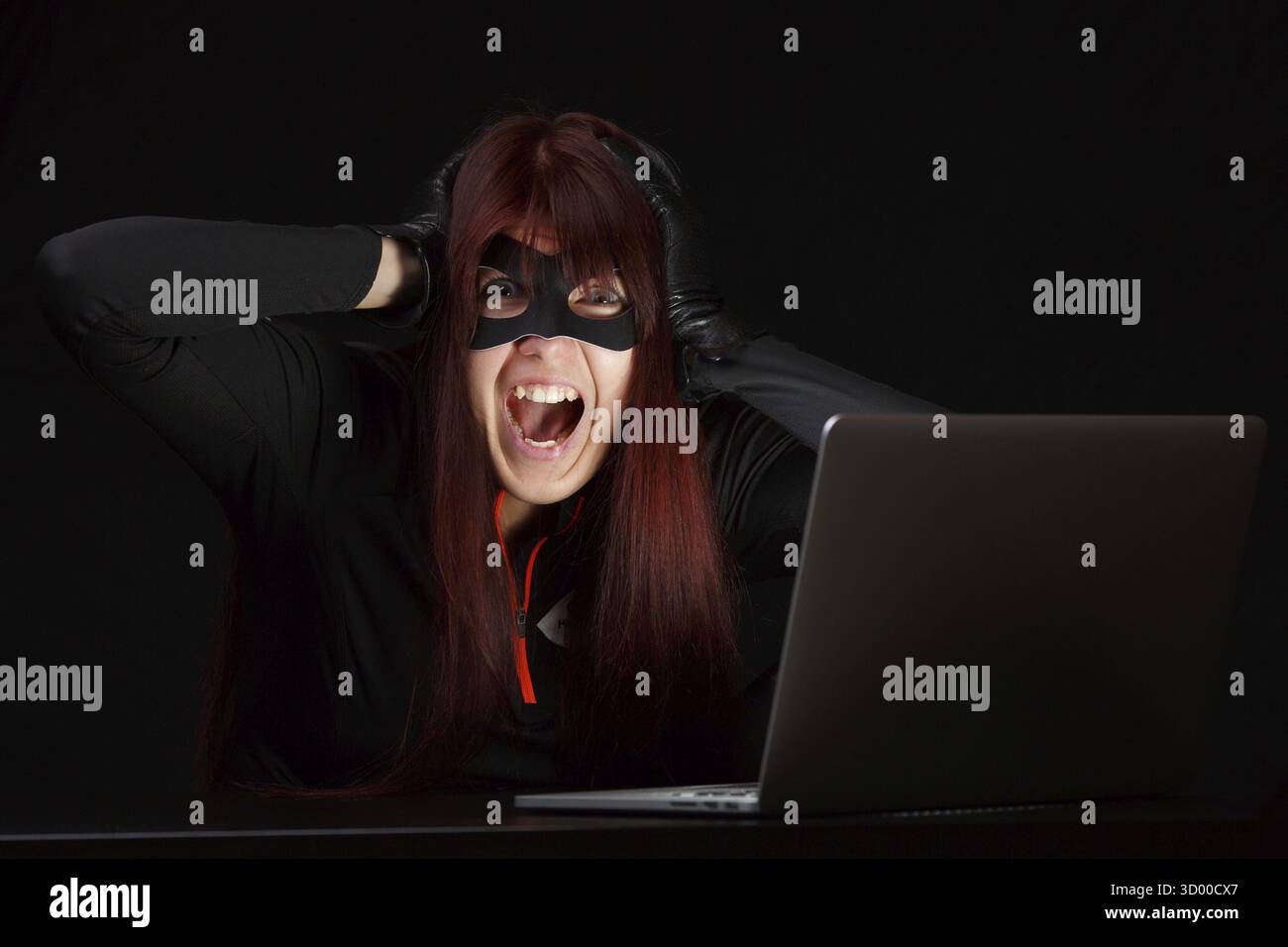 Brunette hacker in black mask screaming at computer Stock Photo