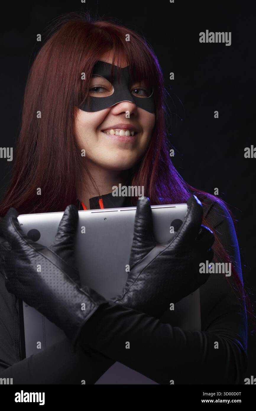 Smiling thief in black gloves holding laptop Stock Photo