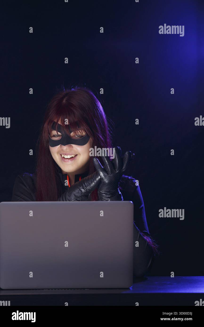 Brunette thief in black mask hacking computer Stock Photo