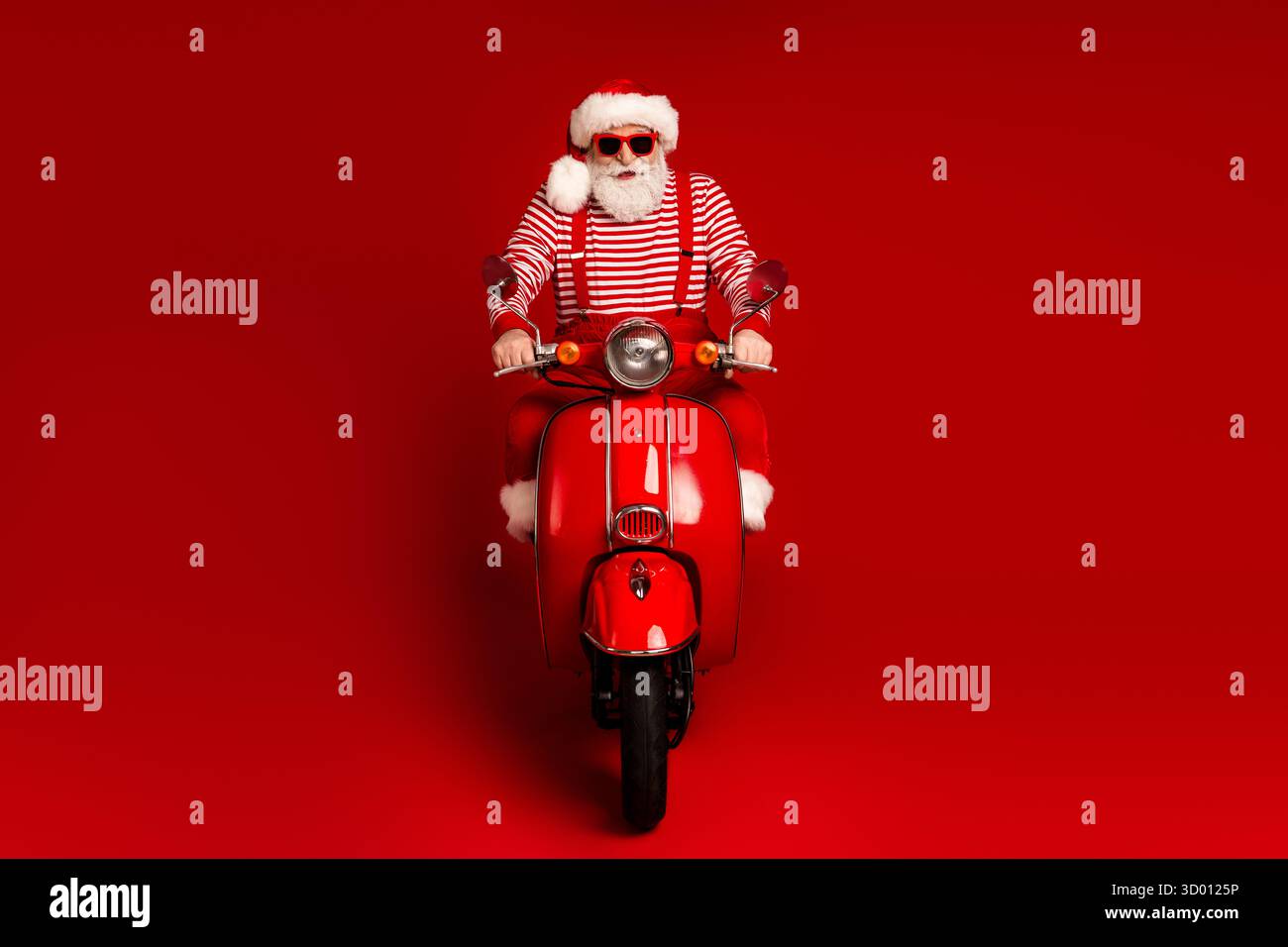 Santa on a red scooter rides against a bold red background in a festive ...