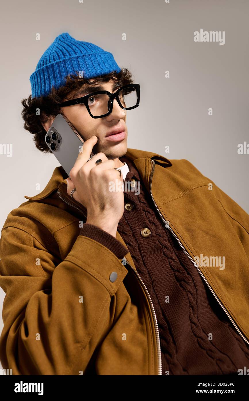 Young handsome man wearing a blue hat and stylish jacket engages in conversation while pondering. Stock Photo