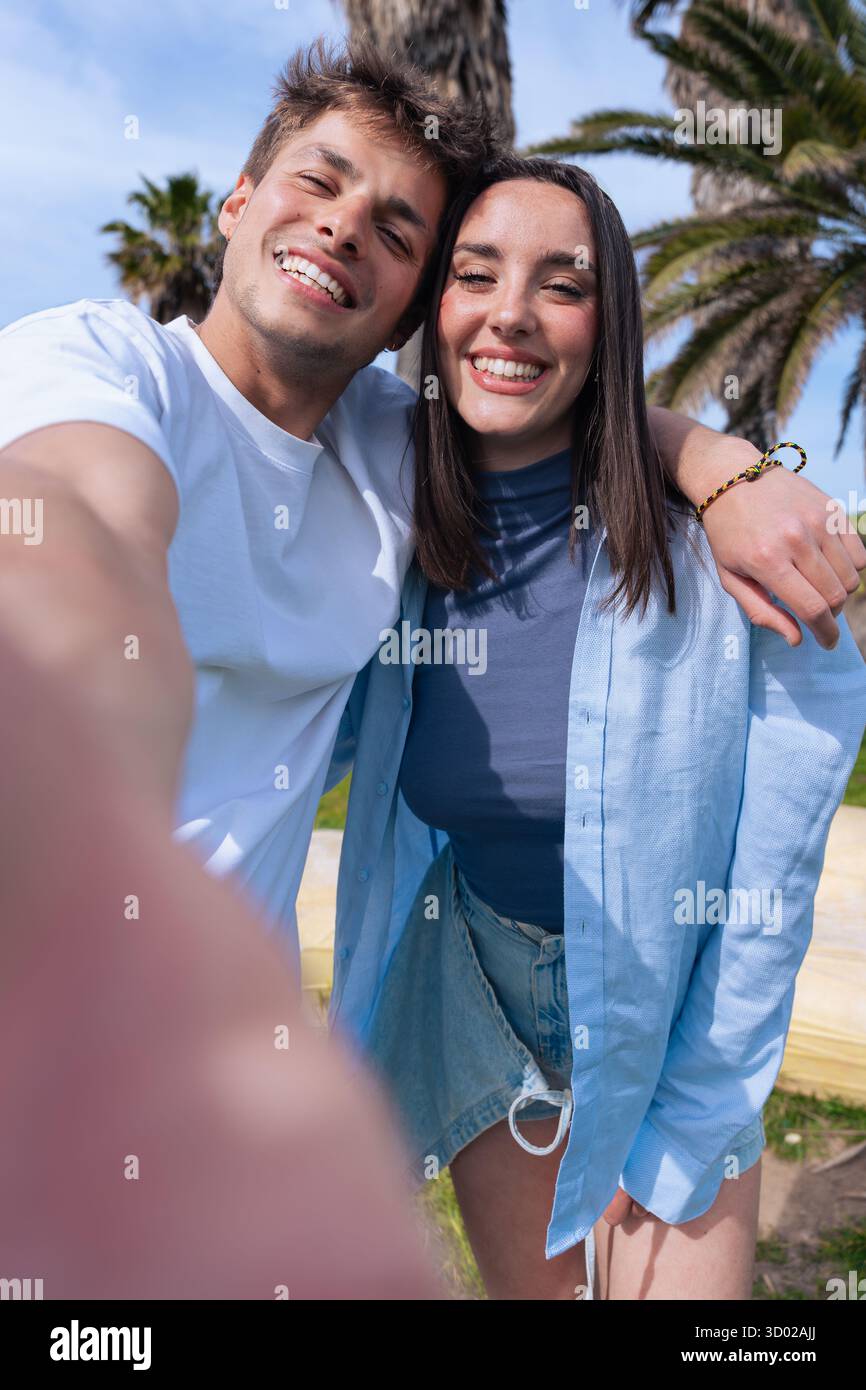 Happy couple taking selfie together at the beach with palm trees in background Stock Photo