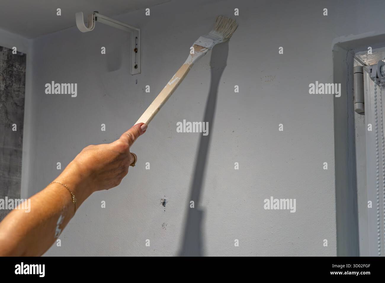 Smiling blonde woman painting wall white with brush during home renovation. Concept of diy project, interior design, home improvement, renovation work Stock Photo