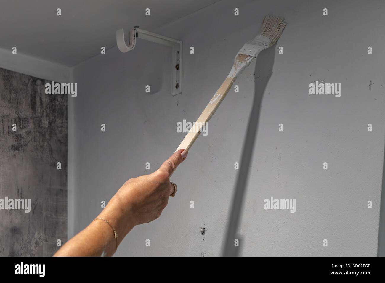 Smiling blonde woman painting wall white with brush during home renovation. Concept of diy project, interior design, home improvement, renovation work Stock Photo