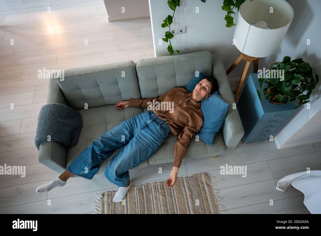 Drained mature woman lies motionless on sofa overwhelmed by mental exhaustion and sorrow at home Stock Photo