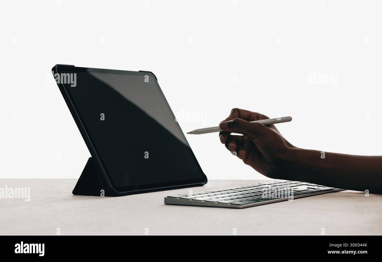 Modern workspace setup featuring a tablet on a stand, keyboard, and a hand using a stylus in a minimal setting, emphasizing technology, creativity, an Stock Photo