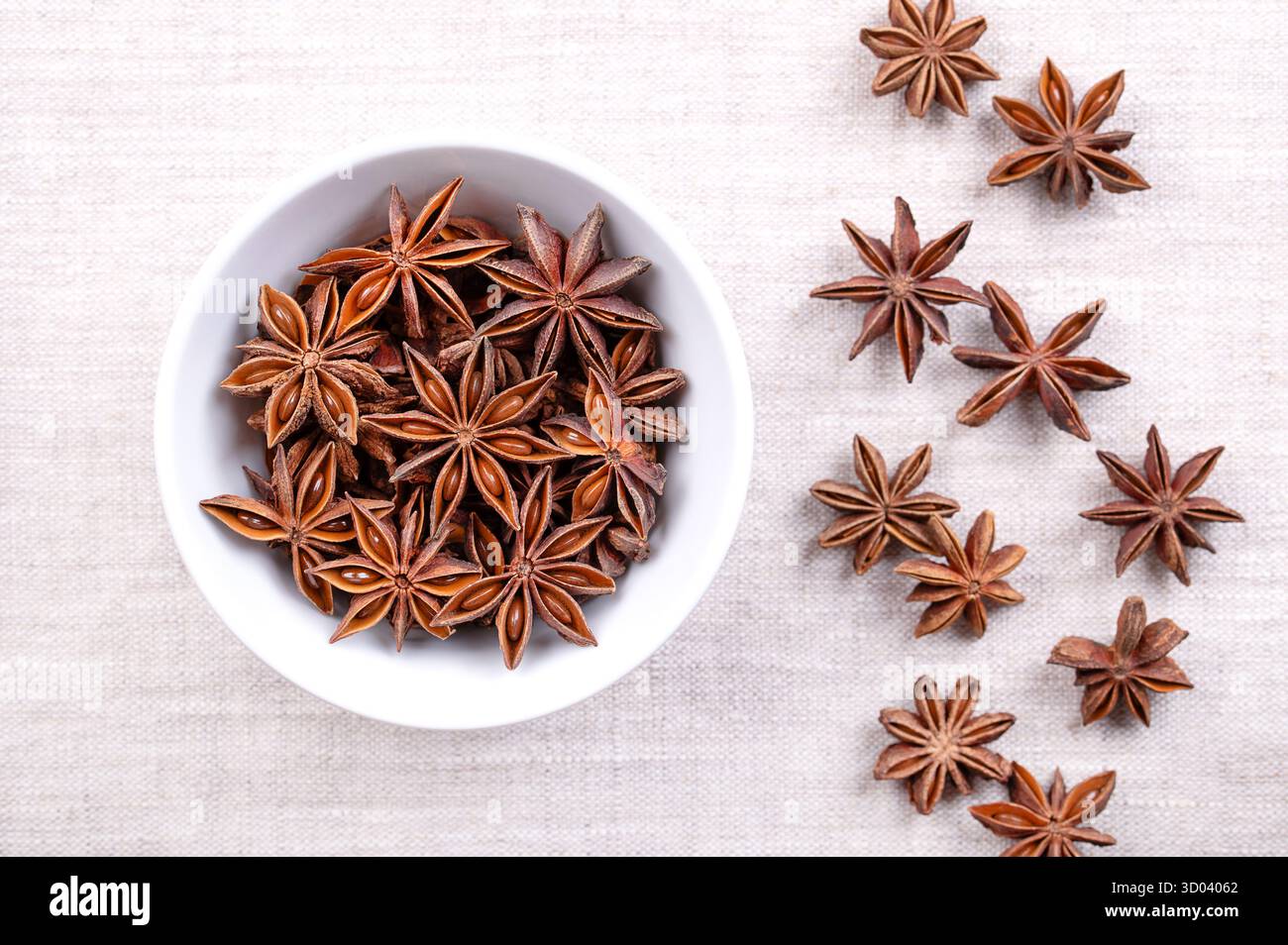 Star anise seeds, fruits and seeds, in a white bowl on linen. Star shaped fruits of Illicium verum, also known as badian, and as star aniseed. Stock Photo