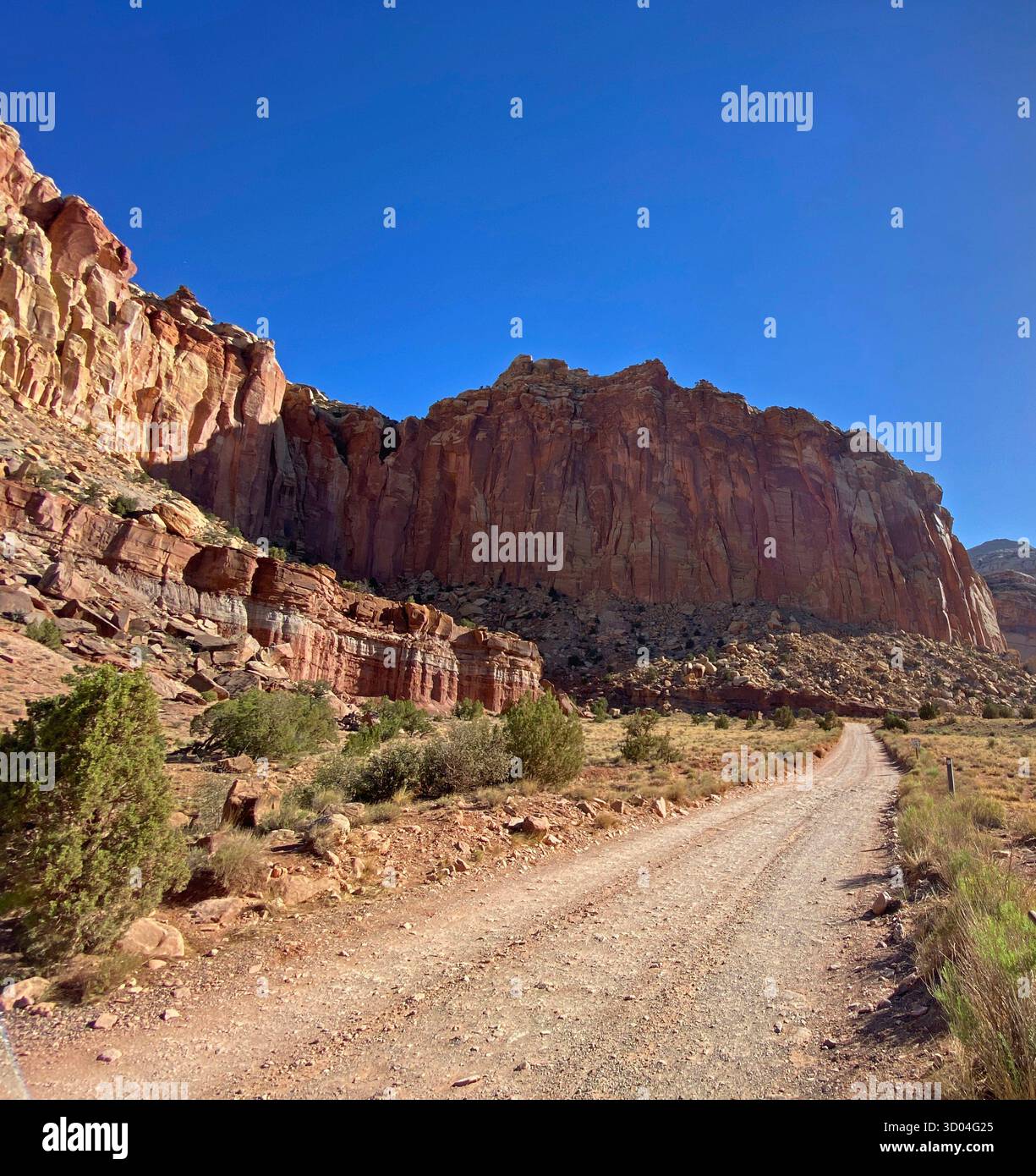 Eroding cliffs of red sandstone and limestone, against a clear blue sky, lining a dirt road, in Capitol Reef National Park, Utah, USA - Smartphone Captured Stock Image