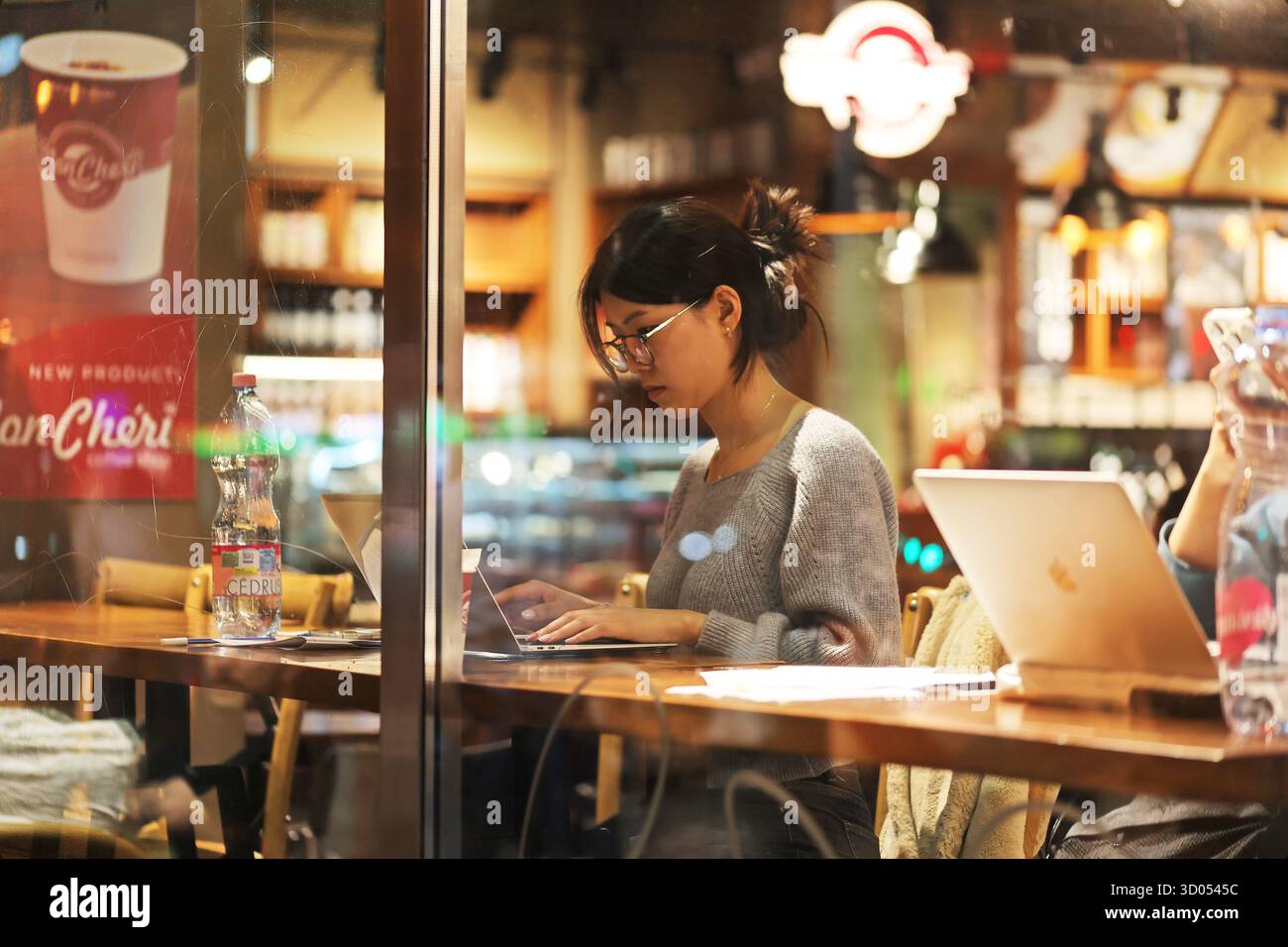 Young woman working on her laptop in a cozy coffee shop during evening Stock Photo