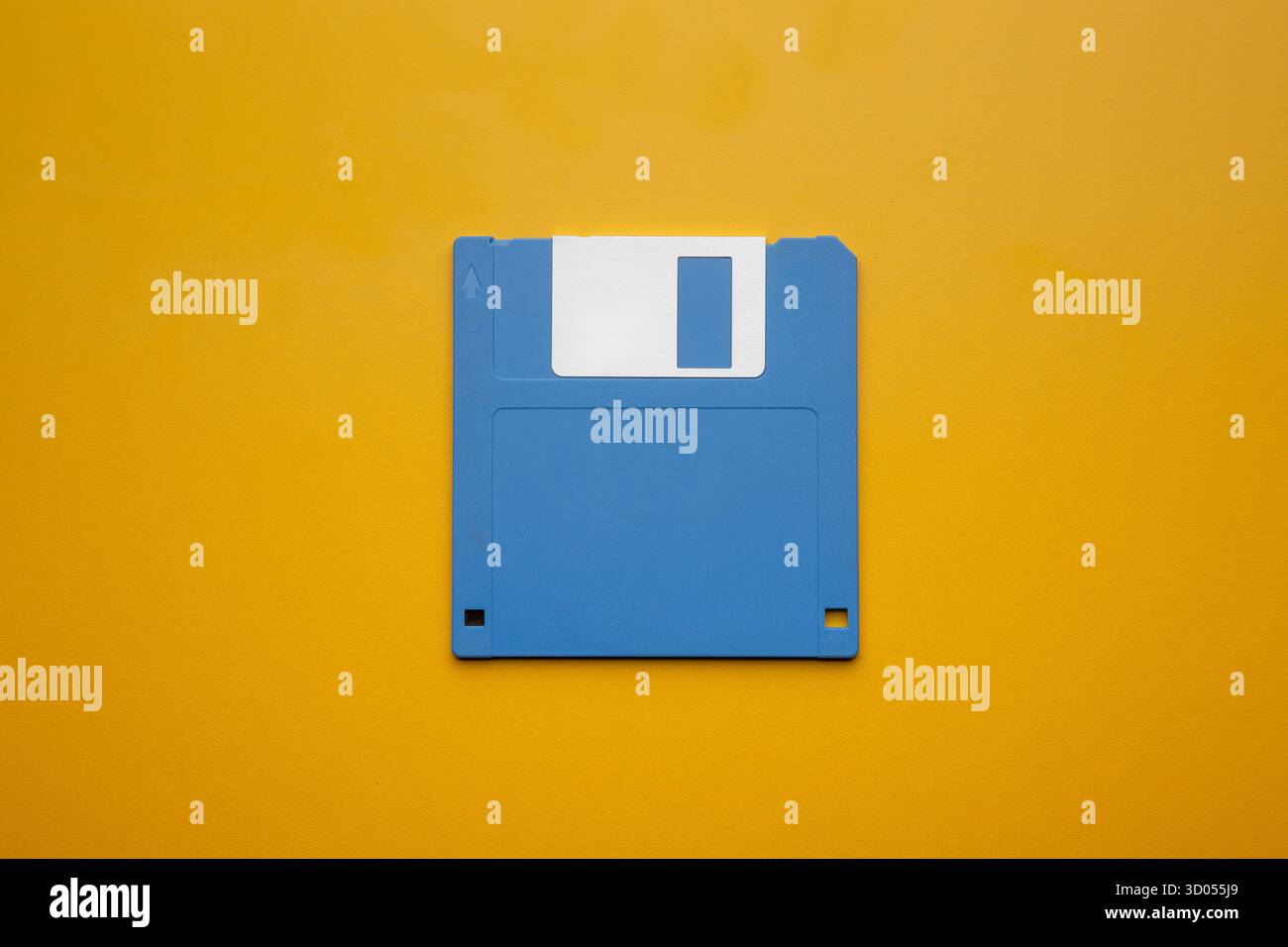 Blue 3.5-inch floppy disk centered on a vibrant yellow background Stock Photo