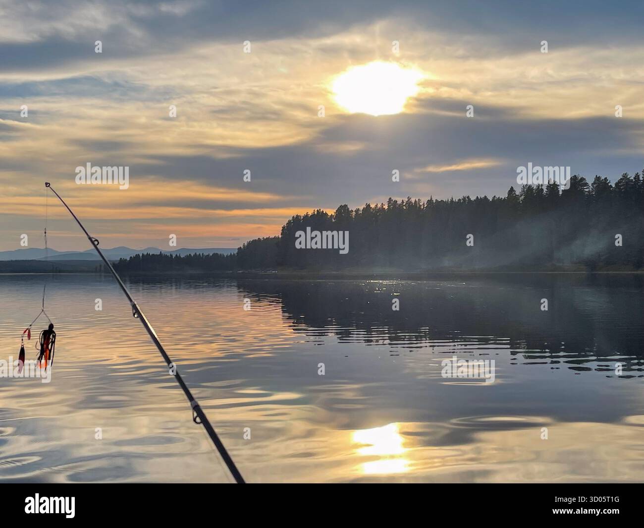 A tranquil lakeside scene at sunset features a angled fishing rod casting a line over glassy water. Reflections of clouds and trees peaceful scenery. - Smartphone Captured Stock Image