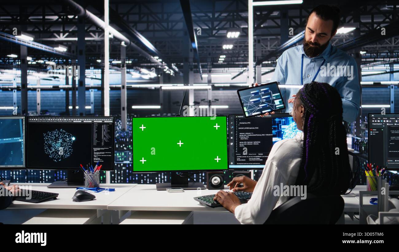Female programmer talking with manager in data center, reviews AI diagnostics on green screen PC. IT expert and supervisor optimizes artificial intelligence systems using mockup computer, camera A Stock Photo
