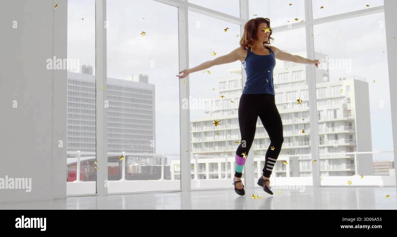 Balancing dancer wearing tank top and colorful leg warmers in studio with confetti and city skyline Stock Photo