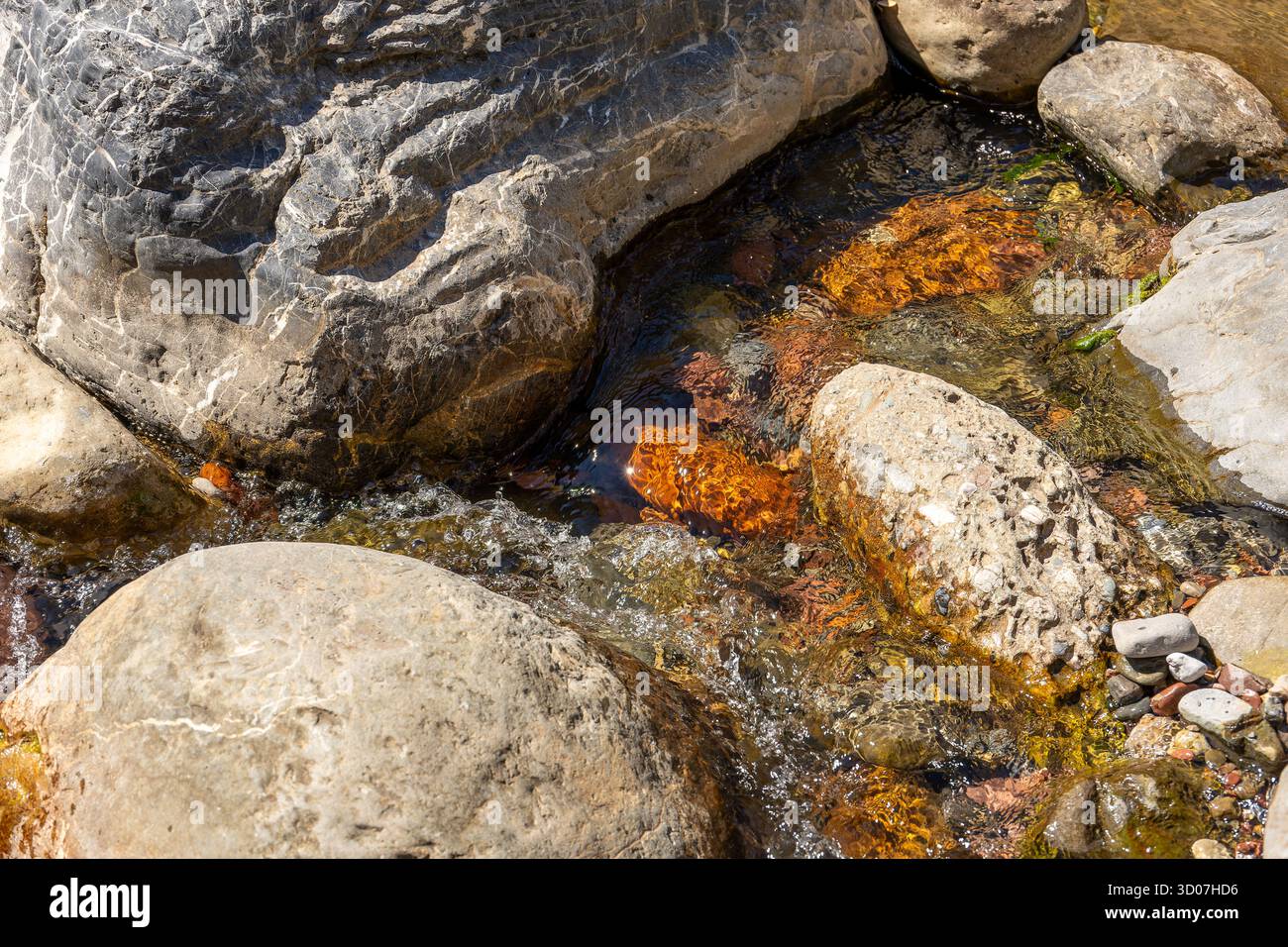 A stream of water flows between large rocks. The water is fresh and ...