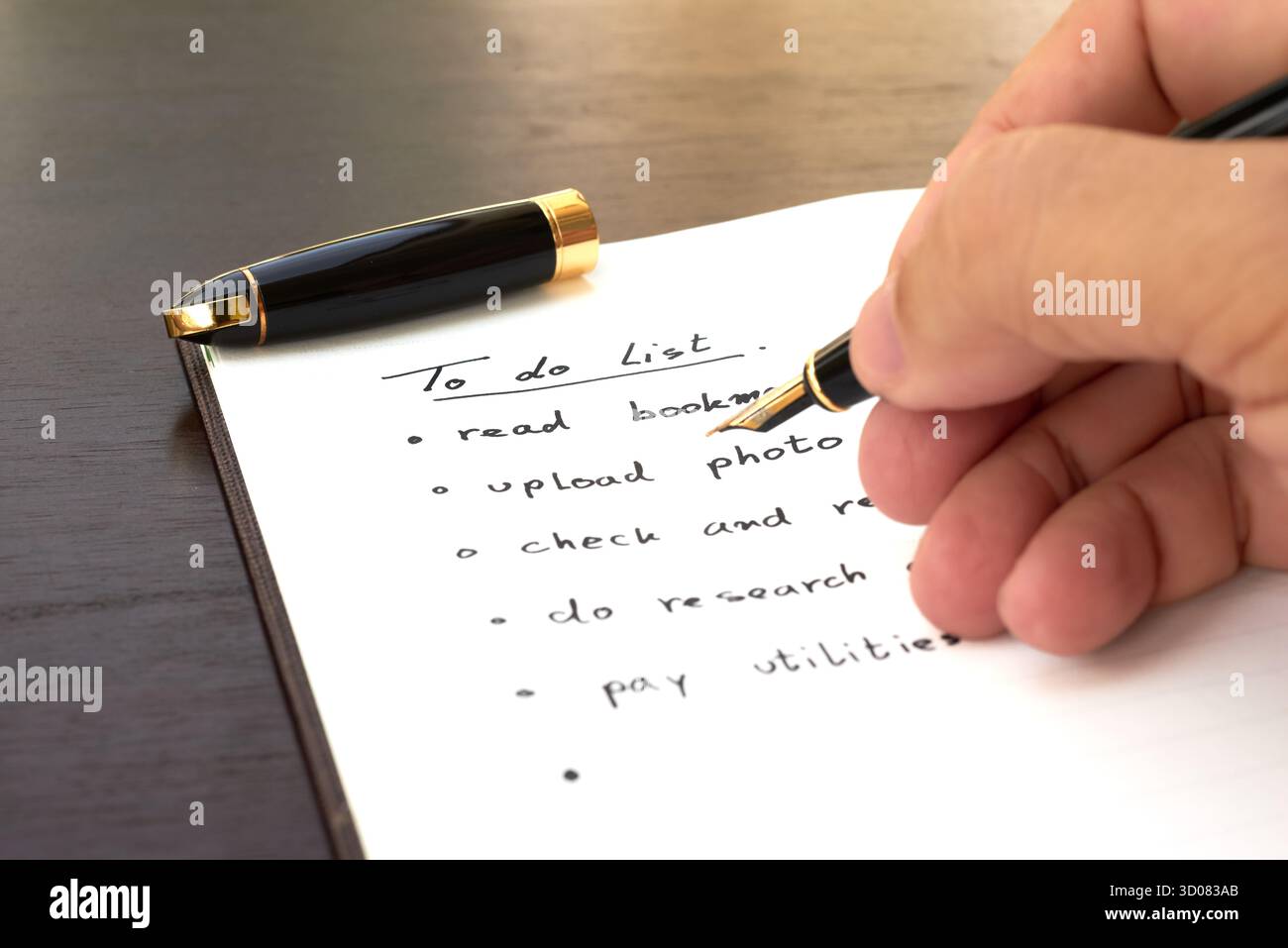 A hand holds a pen above a notebook filled with a to-do list. The list includes tasks like reading, uploading photos, and paying utilities in a simple Stock Photo