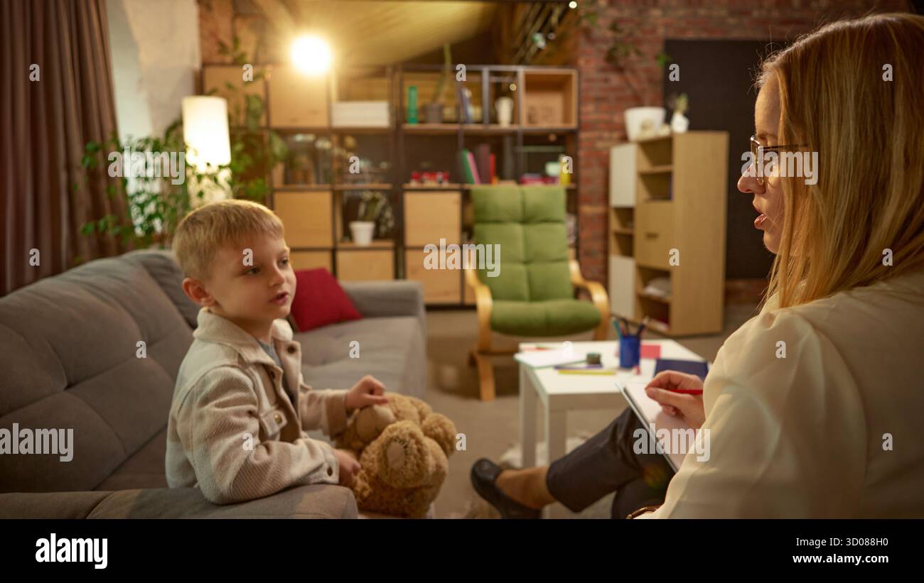 Boy talking with psychologist while holding teddy bear during therapy ...