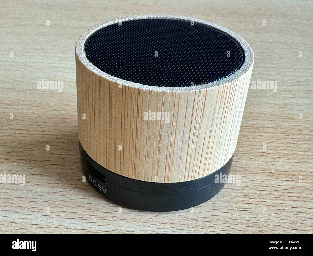 Bamboo Bluetooth speaker on wooden surface showing DC 5V charging port. - Smartphone Captured Stock Image