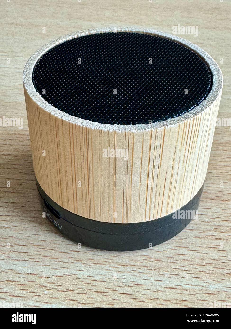 Bamboo Bluetooth speaker on wooden surface showing DC 5V charging port. - Smartphone Captured Stock Image