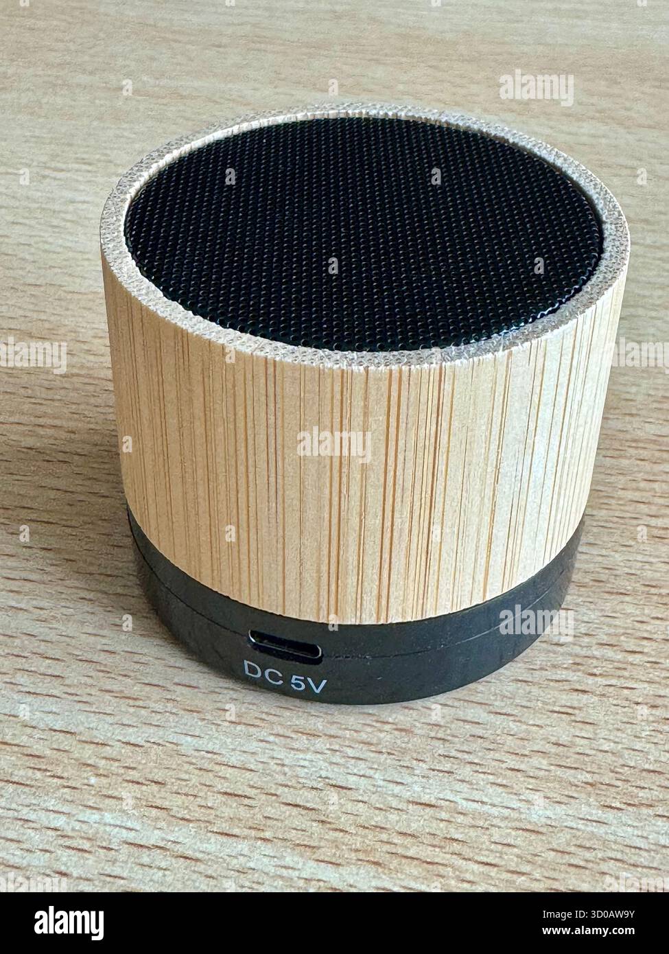 Bamboo Bluetooth speaker on wooden surface showing DC 5V charging port. - Smartphone Captured Stock Image