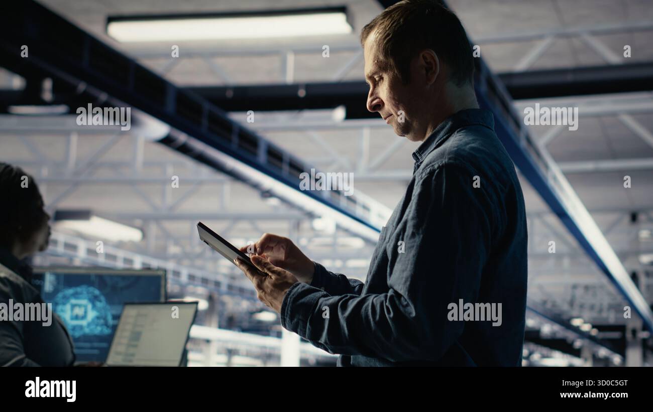 IT expert in server hub uses tablet to optimize deep learning AI systems handling tasks. Data center programmer adjusts artificial intelligence model parameters using device, camera B Stock Photo