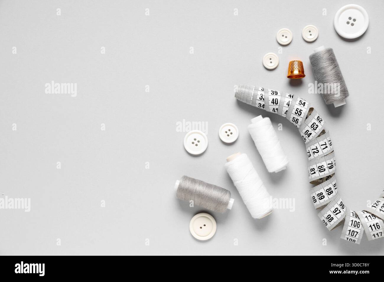 Thread spools with buttons, measuring tape and thimble on grey background Stock Photo