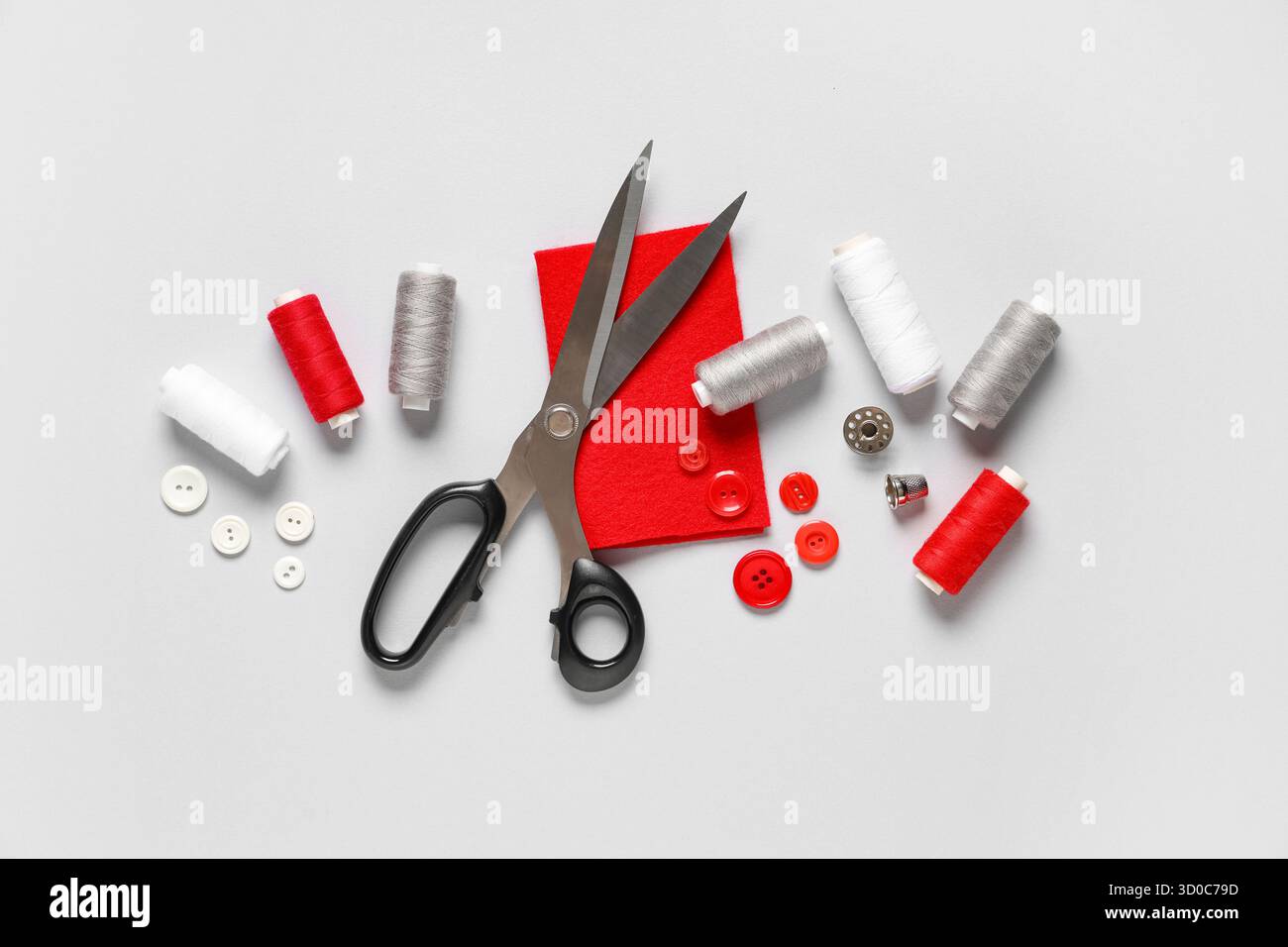 Thread spools with scissors, buttons, fabric and thimble on grey background Stock Photo