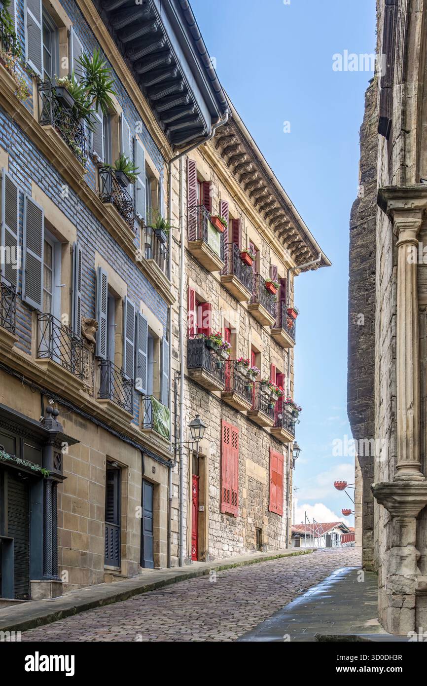 Historic cobblestone street in Hondarribia old town, traditional Basque architecture, colorful shutters, balconies with flowers, stone buildings, Spai Stock Photo
