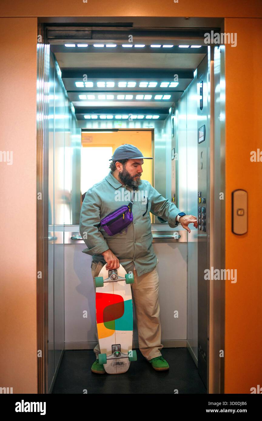 Man holding skateboard inside elevator pressing button. Stock Photo