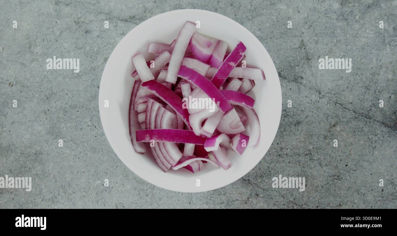 Displaying white bowl containing thinly sliced red onion rings and strips on grey kitchen counter Stock Photo