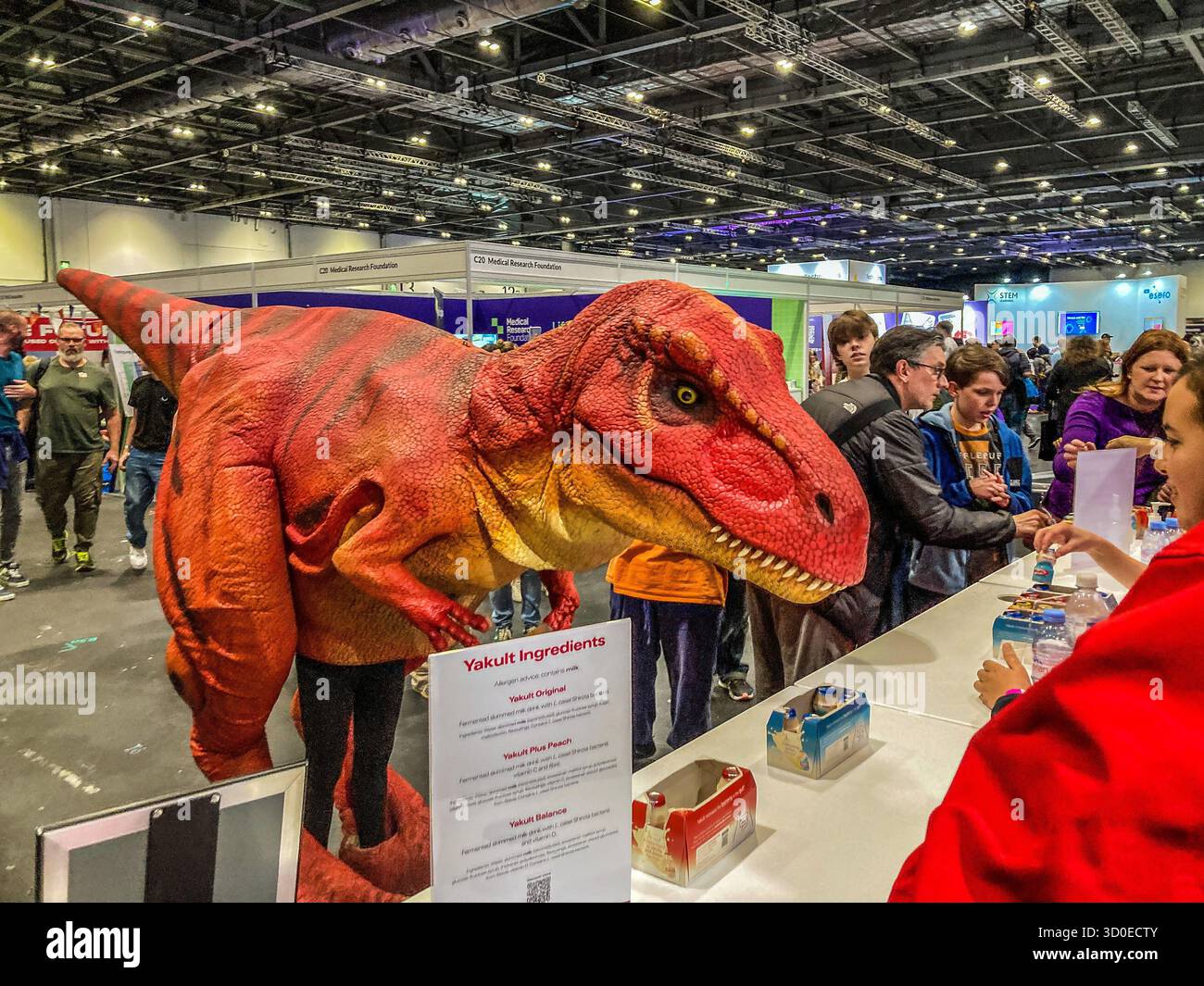 A human-operated puppet of a T-Rex dinosaur visits the Yakult Stand at New Scientist Live,  ExCel, London - Smartphone Captured Stock Image