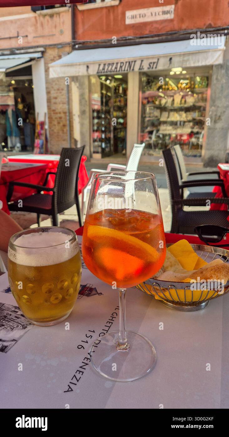Aperol spritz and glass of beer at Italian café in Venice with local shop in background. - Smartphone Captured Stock Image