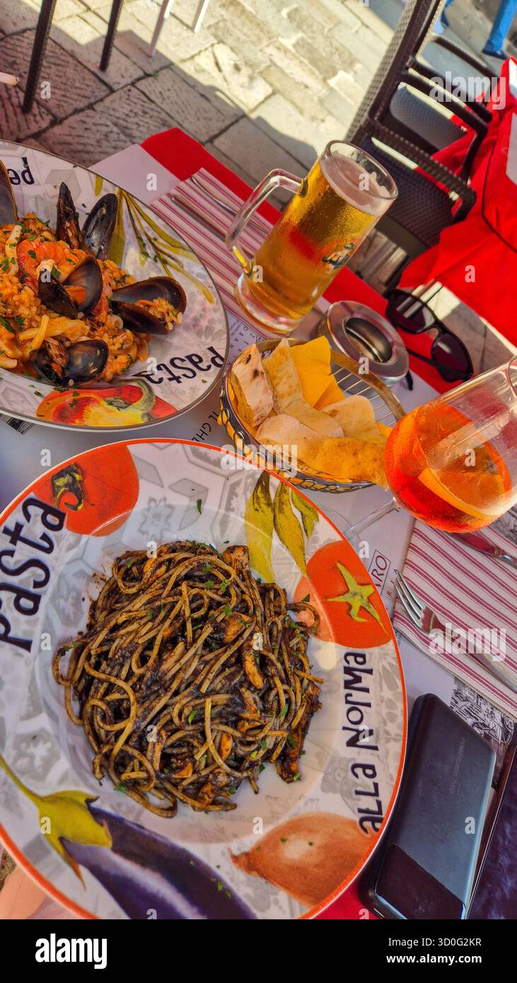 Italian seafood pasta, Aperol spritz and beer served at outdoor café in Venice, Italy, authentic Italian cuisine. - Smartphone Captured Stock Image