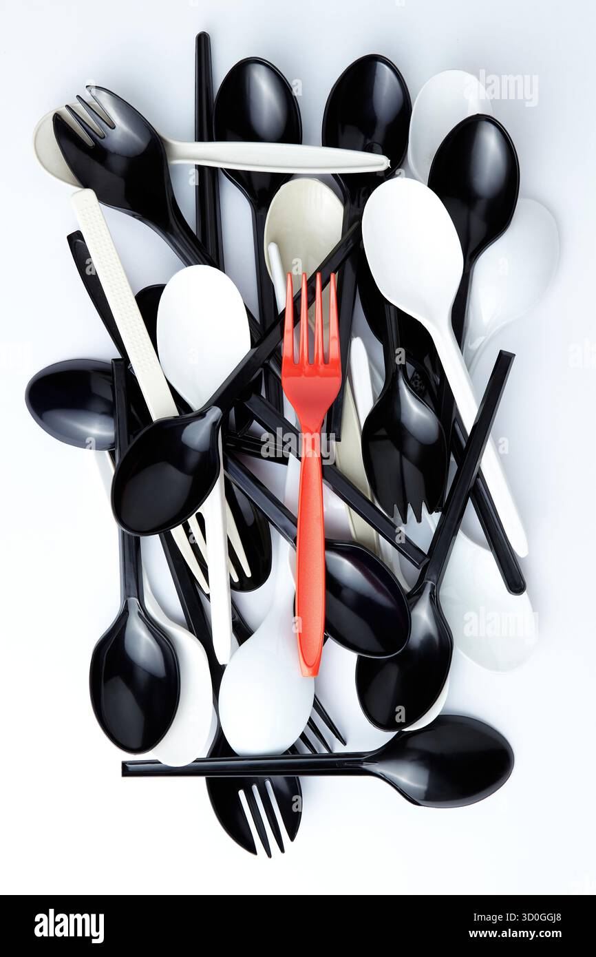 A red plastic fork on top of a pile of black and white plastic spoons and forks Stock Photo