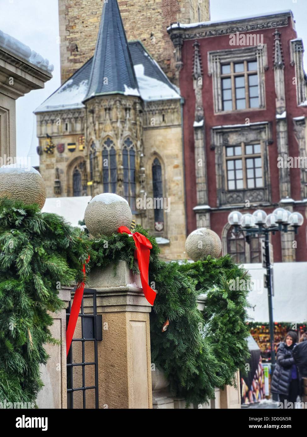 Festive Christmas tree decorated with golden and red ornaments and twinkling lights in front of old gothic towers on a cloudy winter day in a European - Smartphone Captured Stock Image