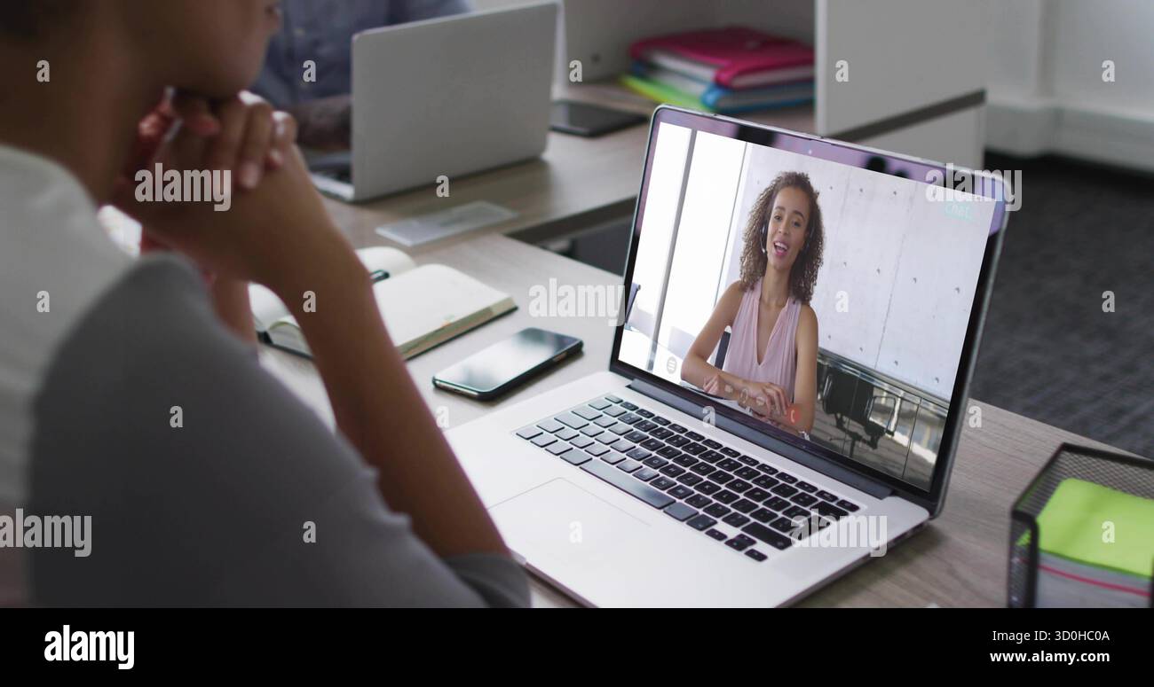 Displaying silver laptop showing woman speaking in virtual call at office, with wire mesh organizer Stock Photo