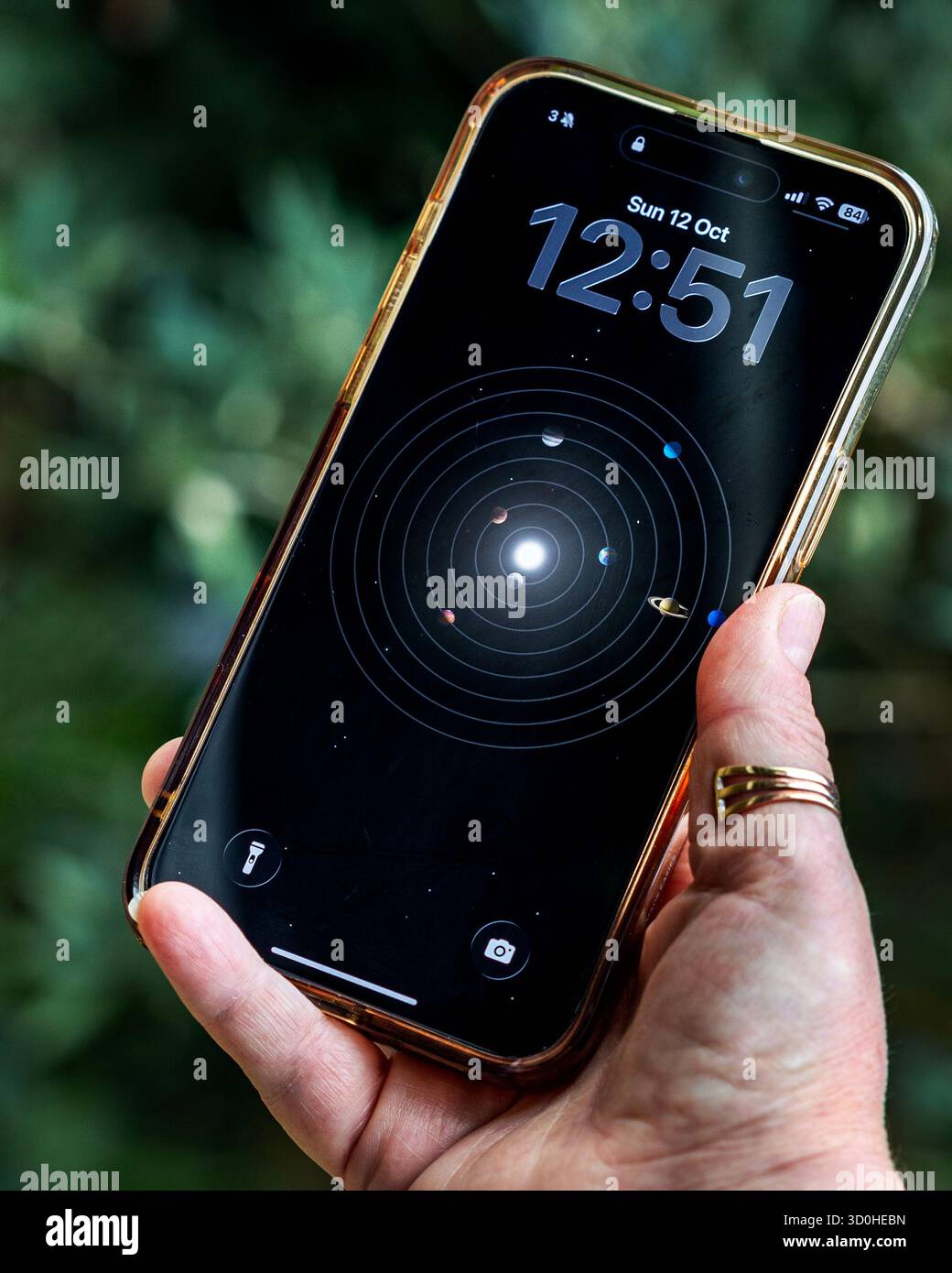 iPhone 15 pro max being held by a caucasion hand, showing the lock screen of planets and the time at 12:51 - Stock Image