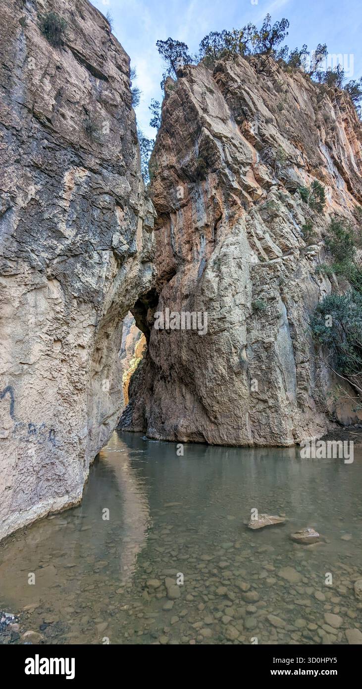 majestic view of a deep gorge with layered rock walls and clear river flowing through a natural arch under daylight - Smartphone Captured Stock Image